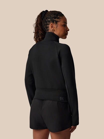 Person wearing a black outfit with a brand logo on a beige background