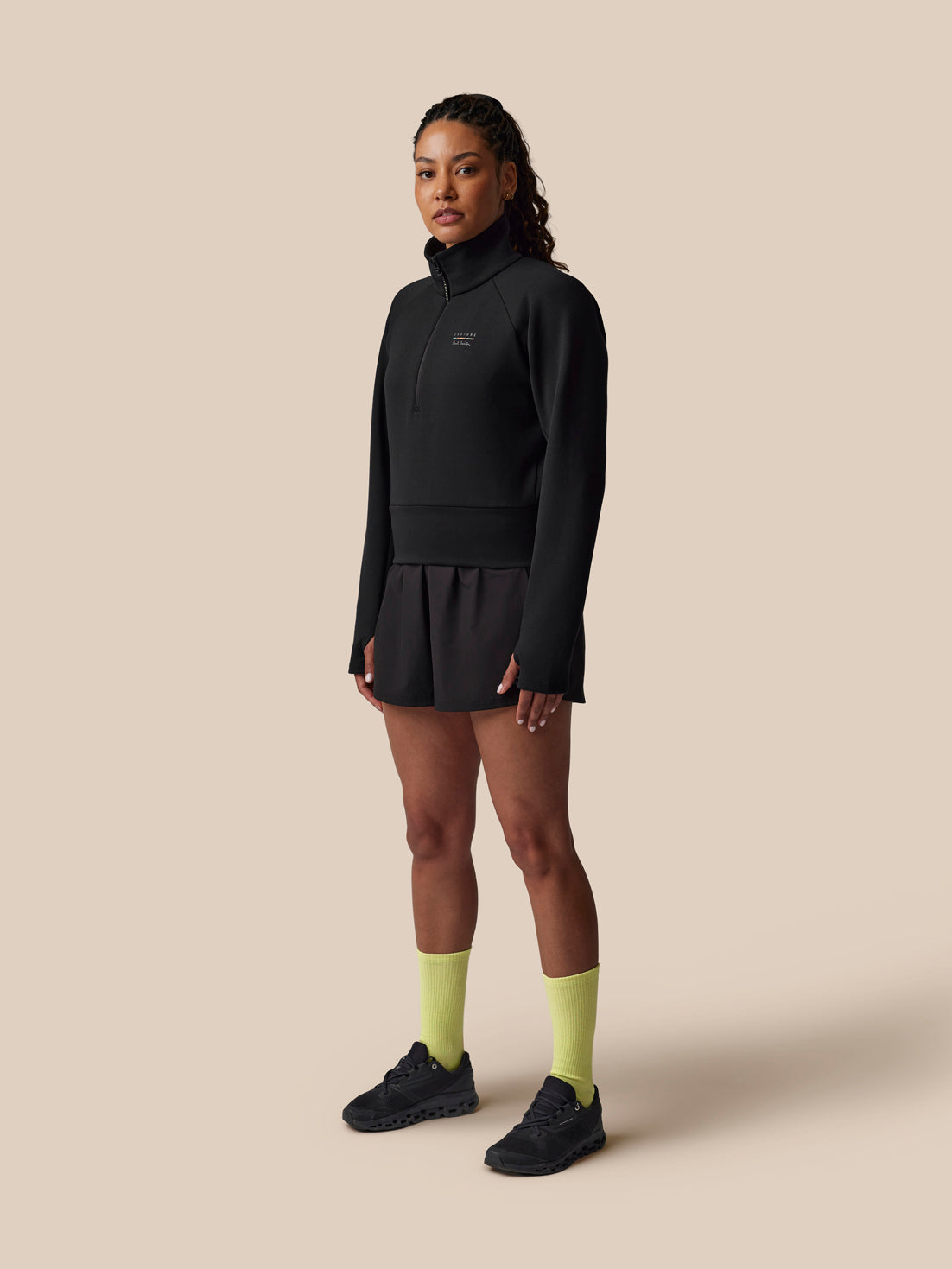 Person wearing a black outfit with yellow socks on a beige background