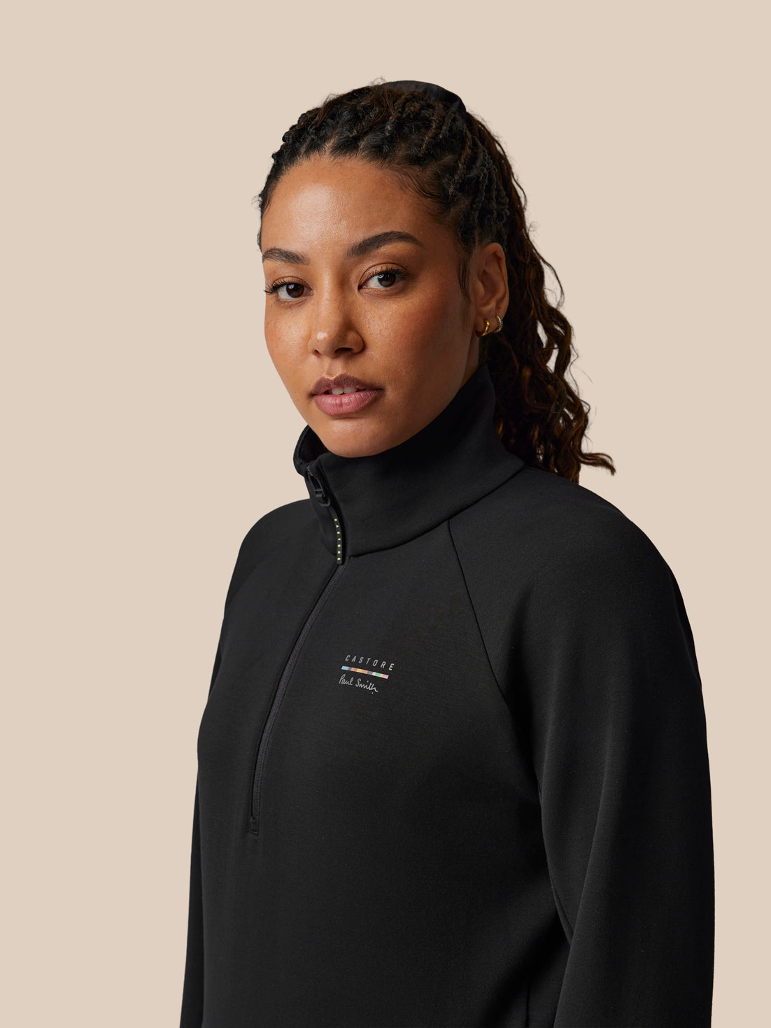 Woman wearing a black high-neck sweatshirt with a brand logo on a beige background