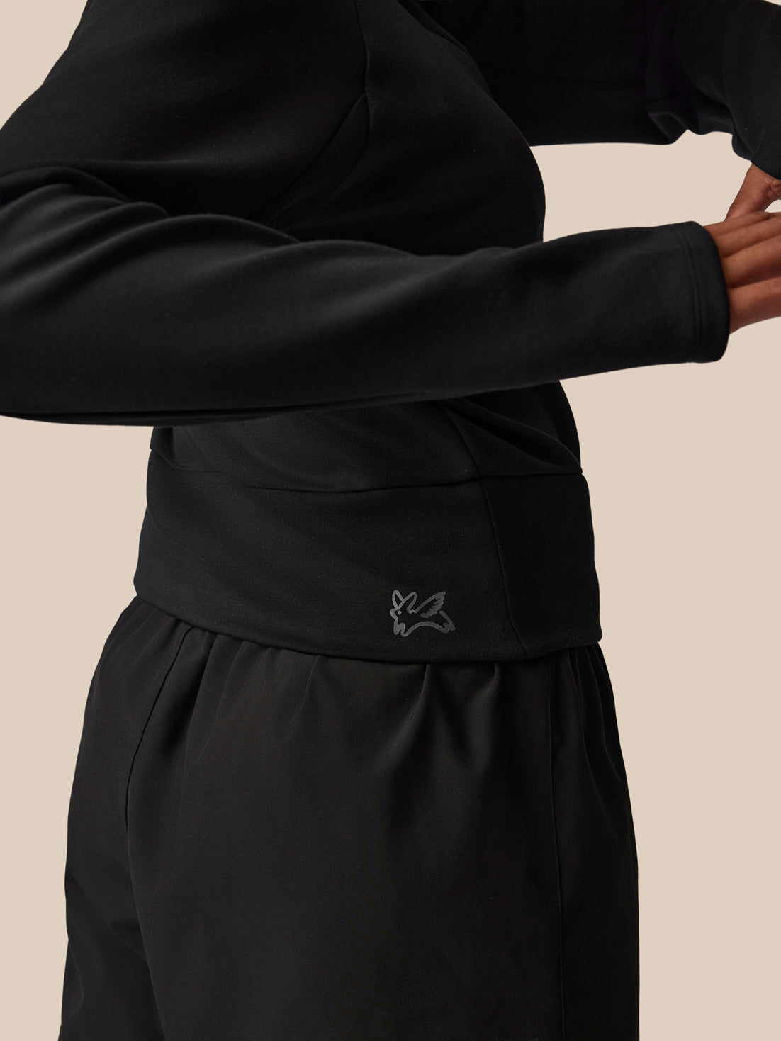Person wearing a black outfit with a brand logo on a beige background