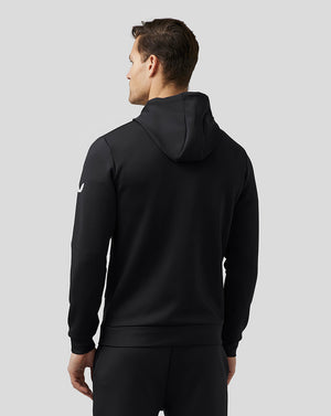 Back view of a man in a black Flex Hoodie, showing the hood and a small emblem on the sleeve.