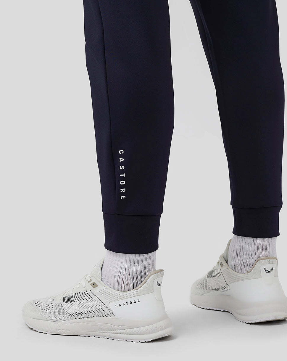 Close-up of navy jogger leg with CASTORE branding along the side and white sneakers.