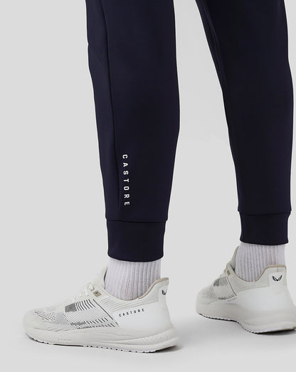 Close-up of navy jogger leg with CASTORE branding along the side and white sneakers.