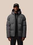Model wearing charcoal puffer jacket with hood, front zip and zipped pockets; Castore logo on left chest and hood.