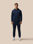 Male model wearing navy travel lifestyle jogger set with hooded zip jacket and matching pants against a beige background