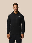 Male model wearing black Travel Lifestyle Hoodie with chest logo against a beige background