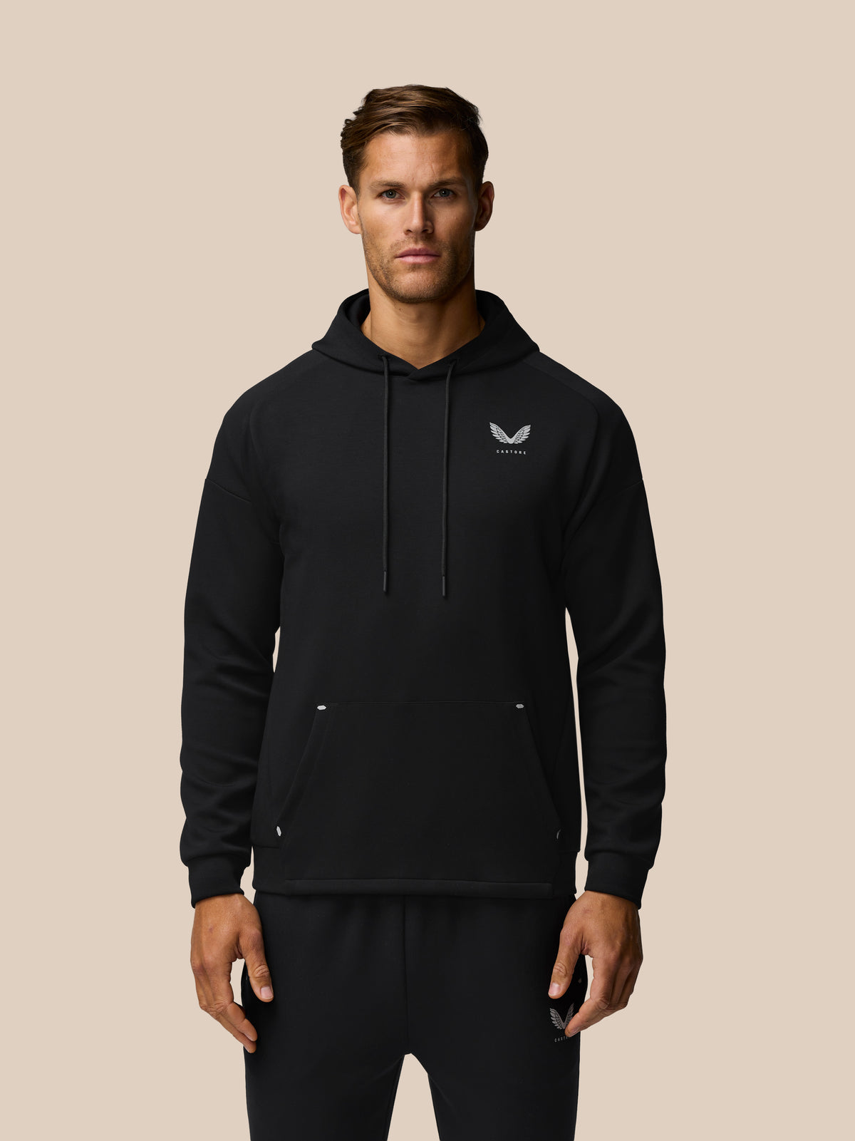 Male model wearing black Travel Lifestyle Hoodie with chest logo against a beige background