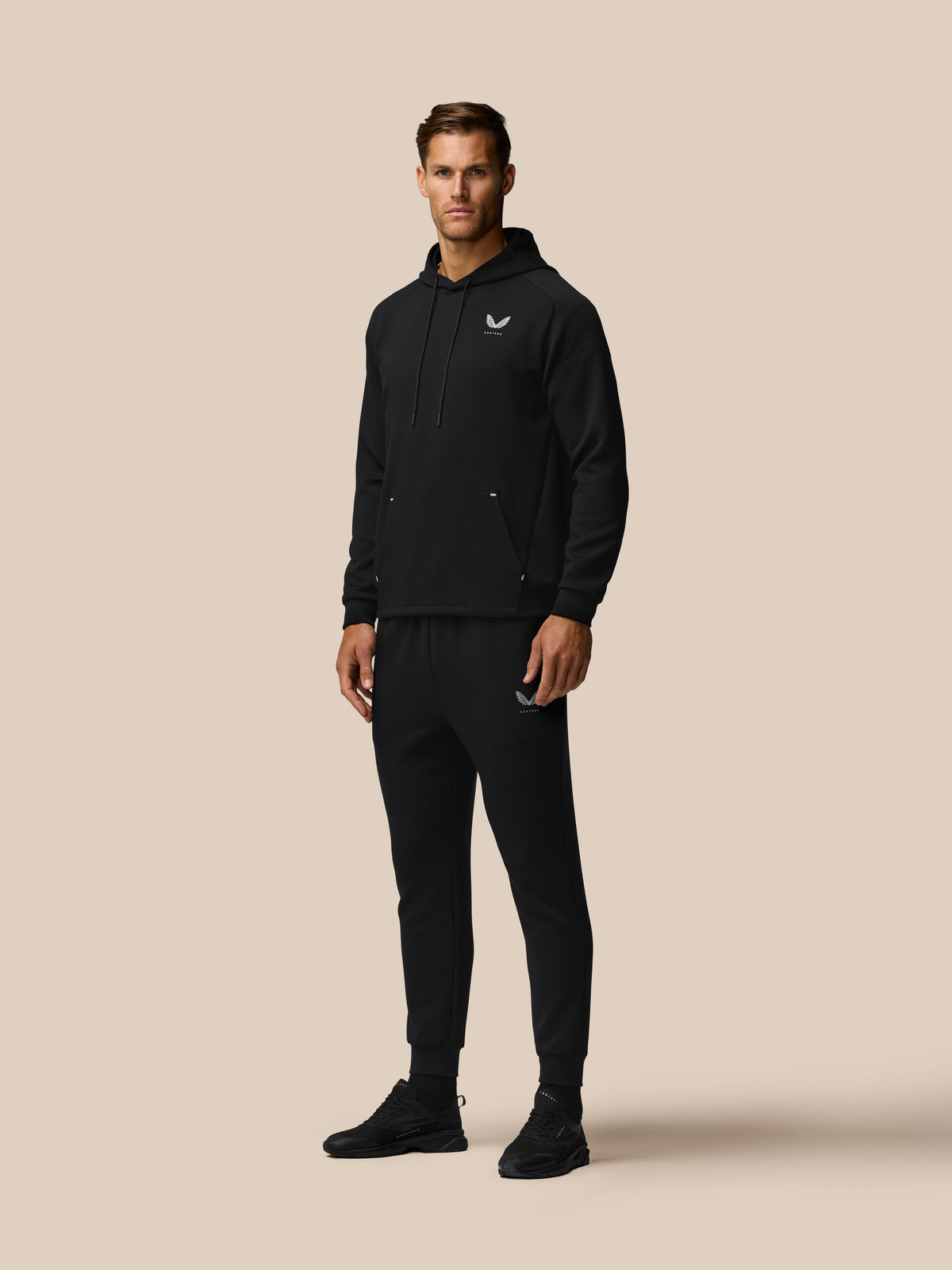 Man wearing black Travel Lifestyle Hoodie with drawstring hood, front kangaroo pocket, and Castore logo on chest