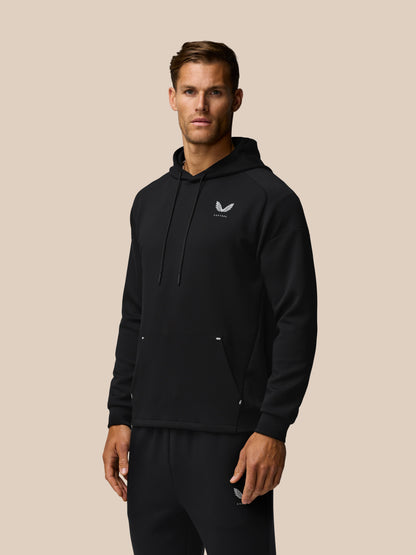 Male model in black Travel Lifestyle Hoodie shown slightly angled, chest logo and drawstring hood visible