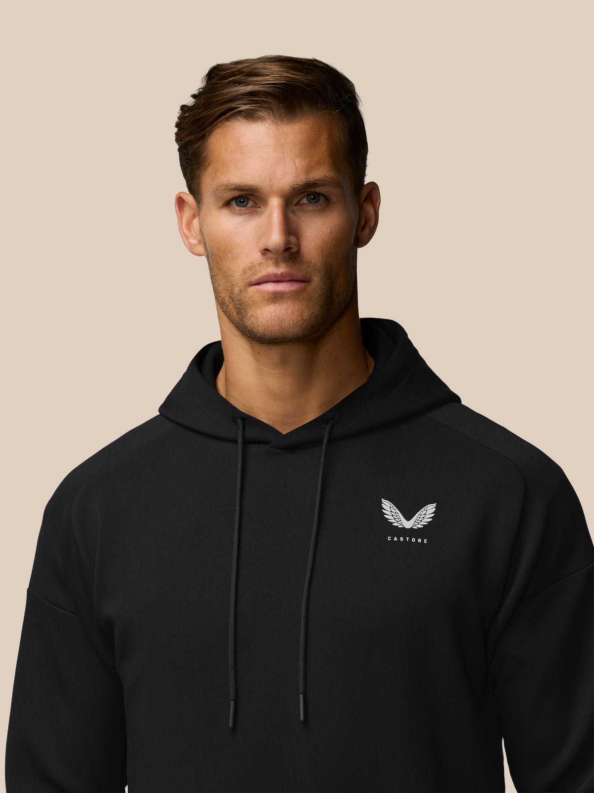 Male model wearing black Travel Lifestyle Hoodie with Castore logo on chest against a beige background