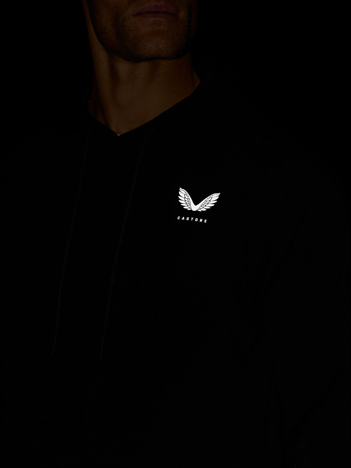 Close-up of white Castore wing logo on the chest of a black Travel Lifestyle Hoodie