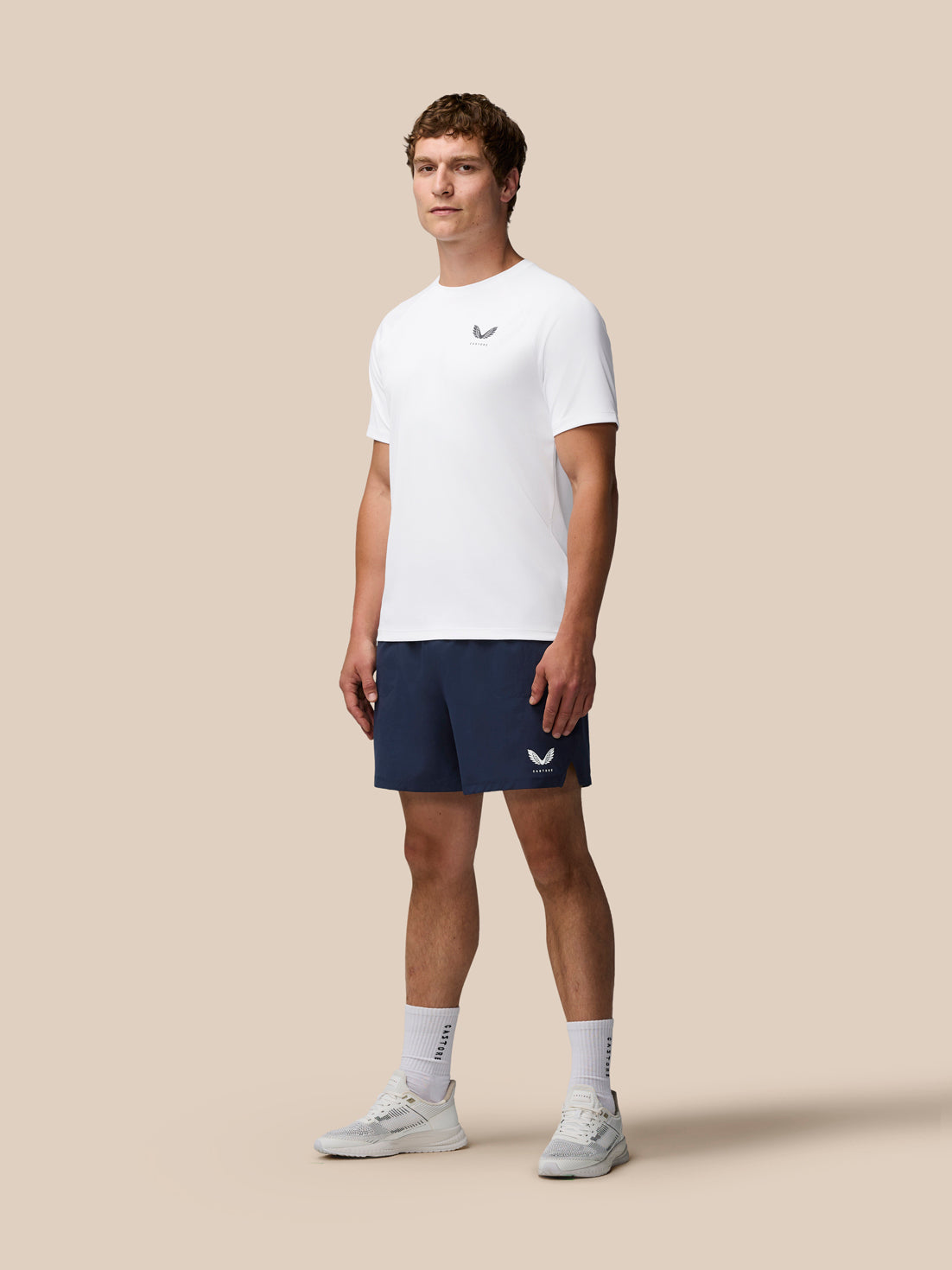 Man wearing a white t-shirt and navy shorts with a logo on a beige background