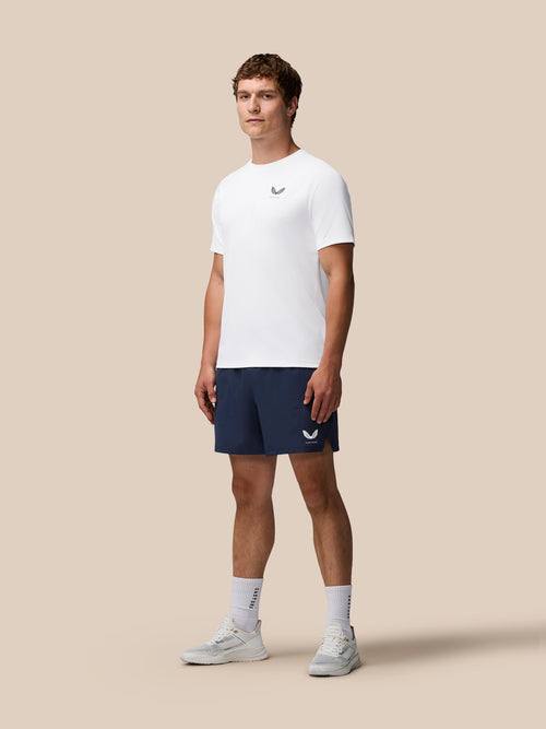 Man wearing a white t-shirt and navy shorts with a logo on a beige background