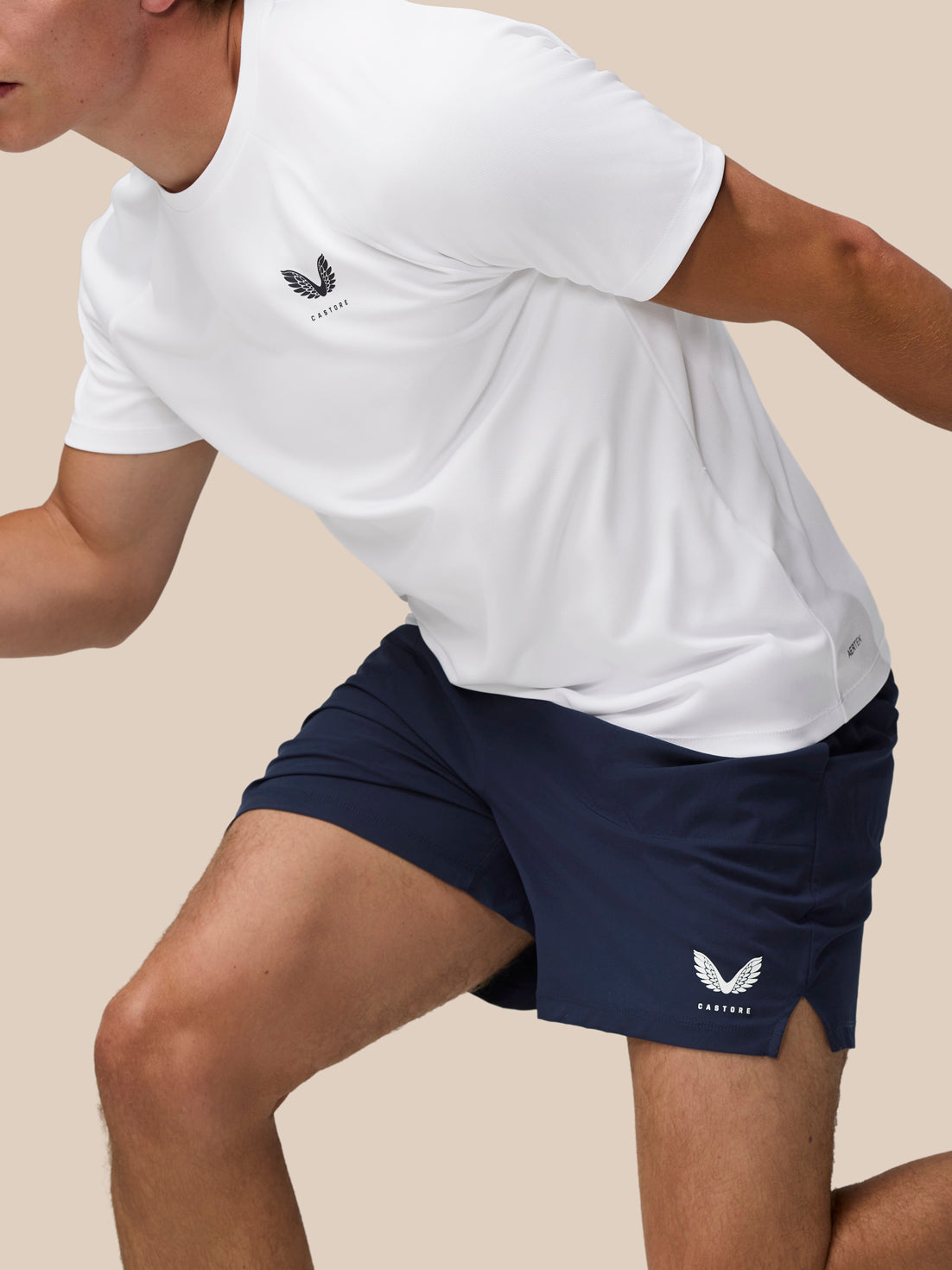 Person wearing a white t-shirt and navy shorts with a brand logo on a beige background