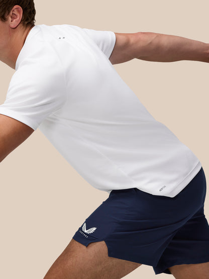 Person wearing a white t-shirt and navy shorts with a logo on a beige background