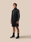 Man wearing black Apex Training Gilet over a gray top, posing against beige background.
