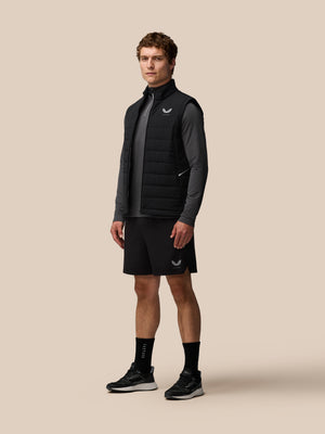 Man wearing black Apex Training Gilet over a gray top, posing against beige background.