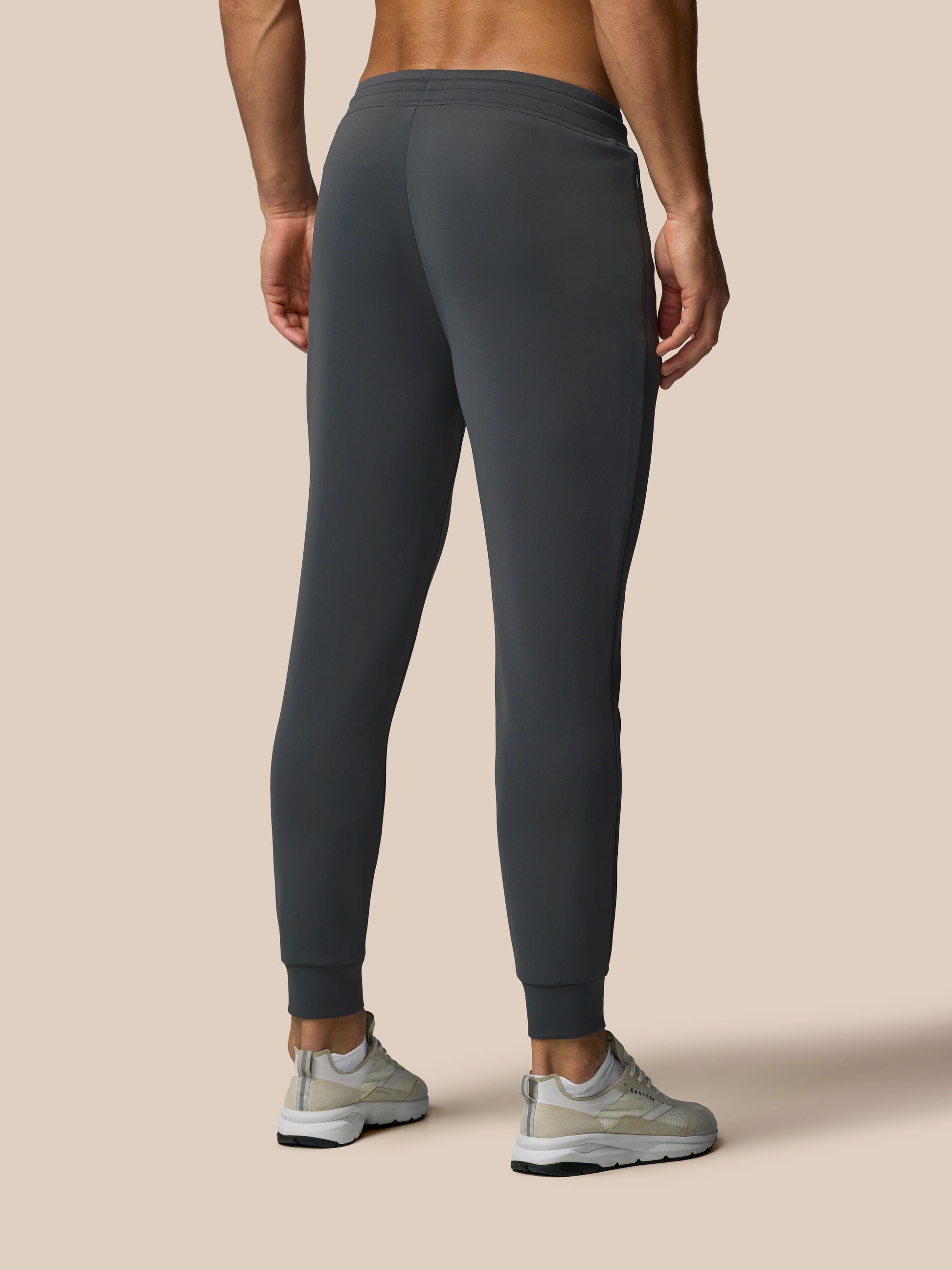 Person wearing dark gray sweatpants on a beige background