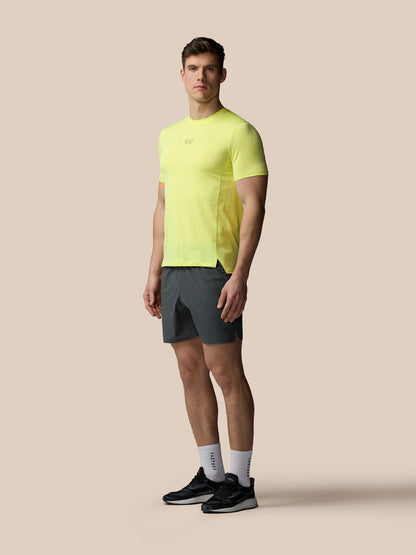 Man wearing a bright yellow athletic shirt and gray shorts on a beige background