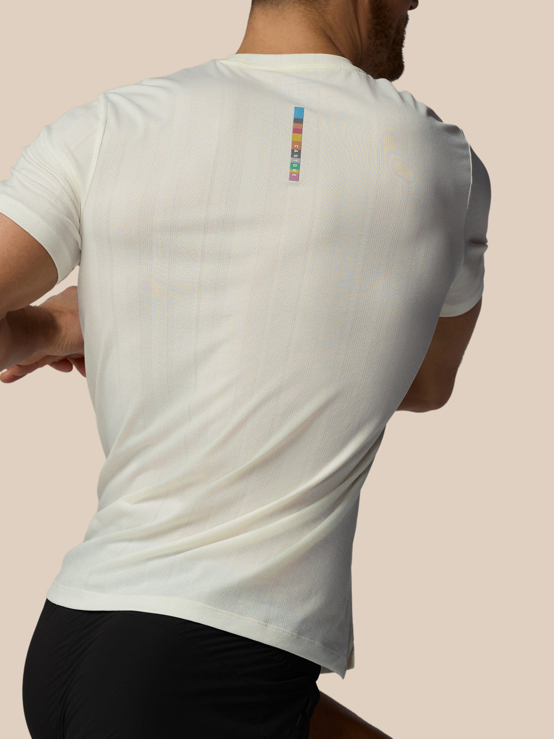 Person wearing a white t-shirt with a colorful logo on the back against a beige background