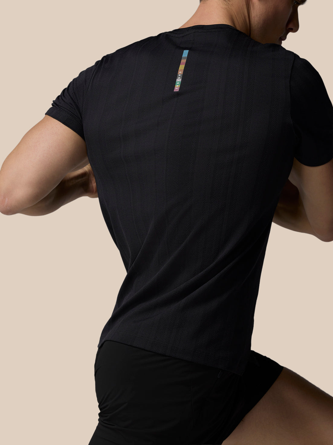 Person wearing a black athletic outfit with a colorful logo on the back against a beige background