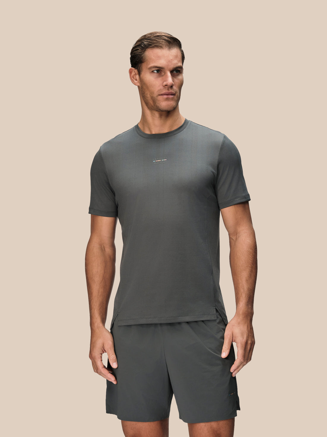 A man modeling a dark gray athletic t-shirt and matching shorts against a solid beige background.
