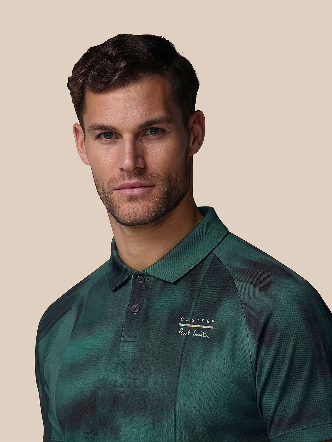Man wearing a green polo shirt with a brand logo on a beige background