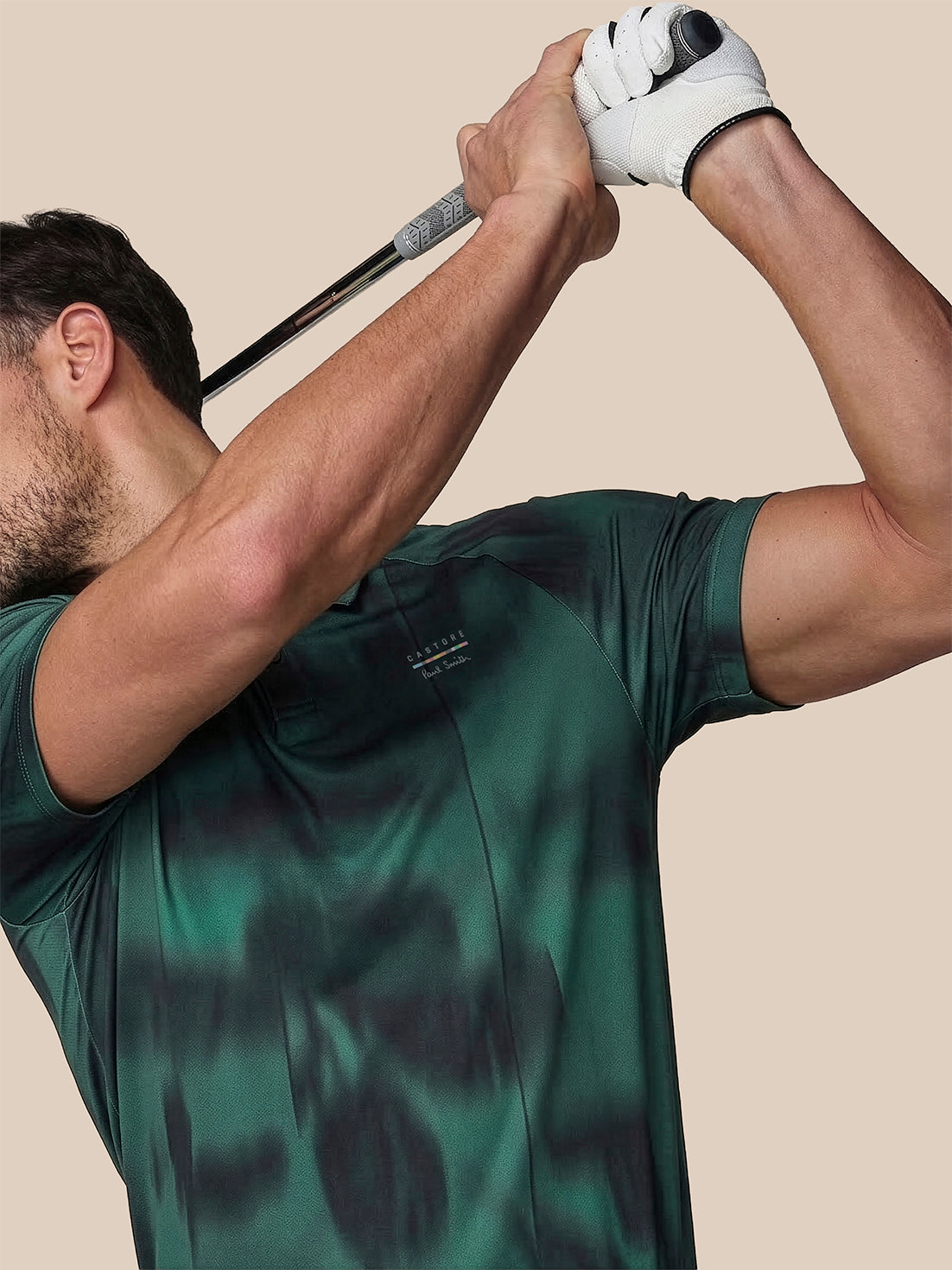 Man in a green shirt swinging a golf club against a beige background
