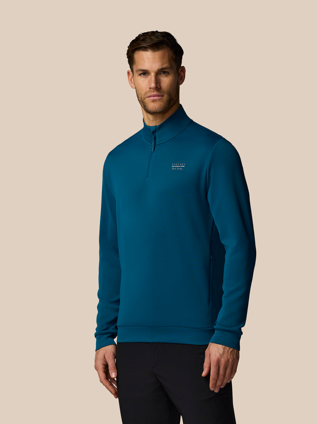 Man wearing a blue pullover with a logo on a beige background