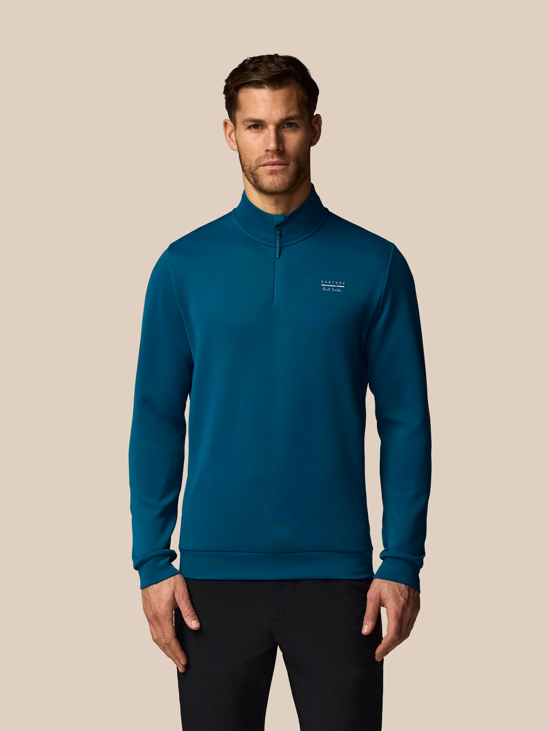 Man wearing a blue pullover with a visible brand logo on a beige background
