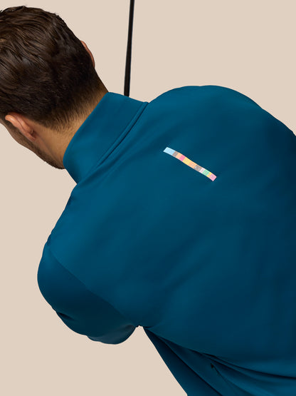 Person wearing a blue jacket with a colorful logo on the chest against a beige background