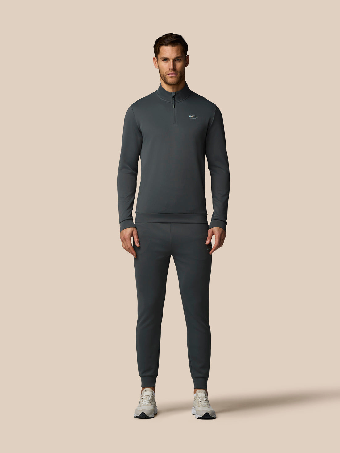 Man wearing a dark gray tracksuit on a beige background