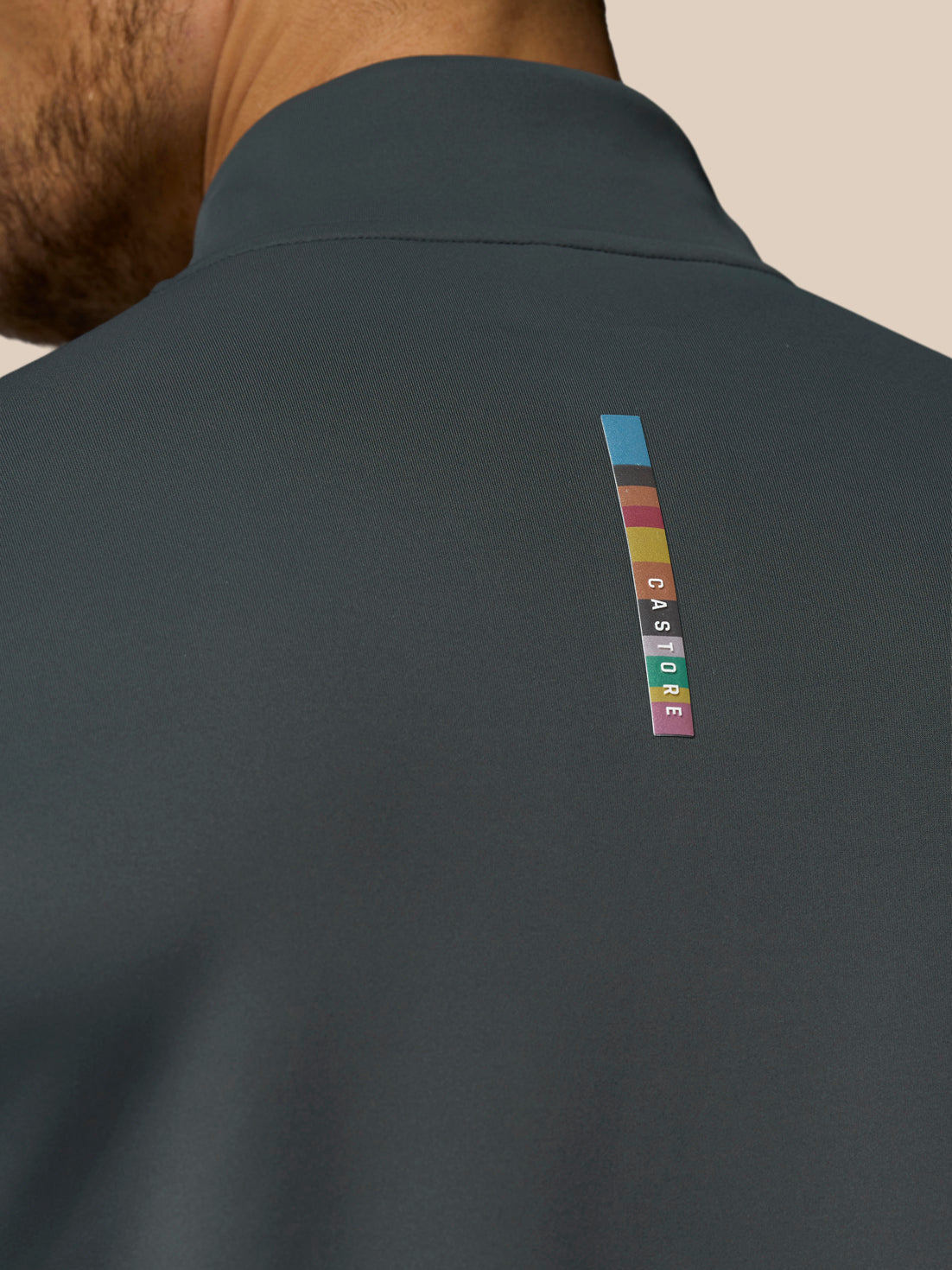 Dark gray jacket with a colorful brand logo on the back against a beige background
