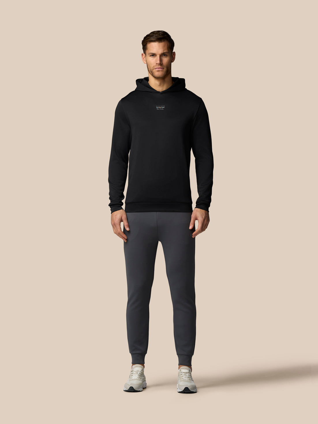 Man wearing a black hoodie and gray pants on a beige background