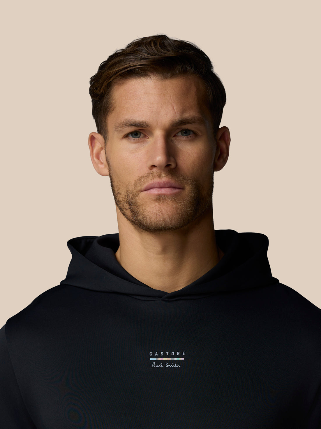 Man wearing a black hoodie with a brand logo on a beige background