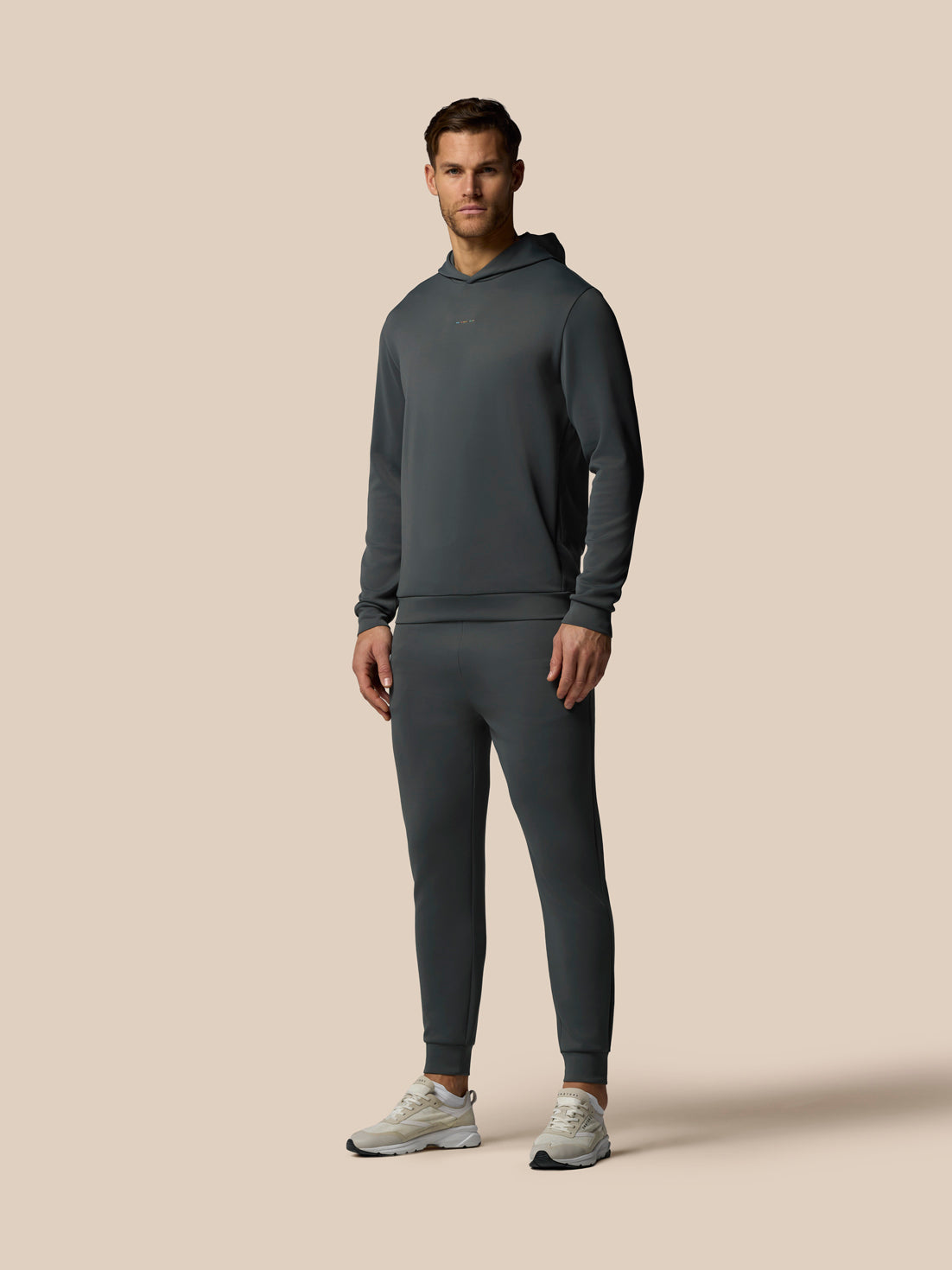 Man wearing a dark gray hoodie and matching pants on a beige background