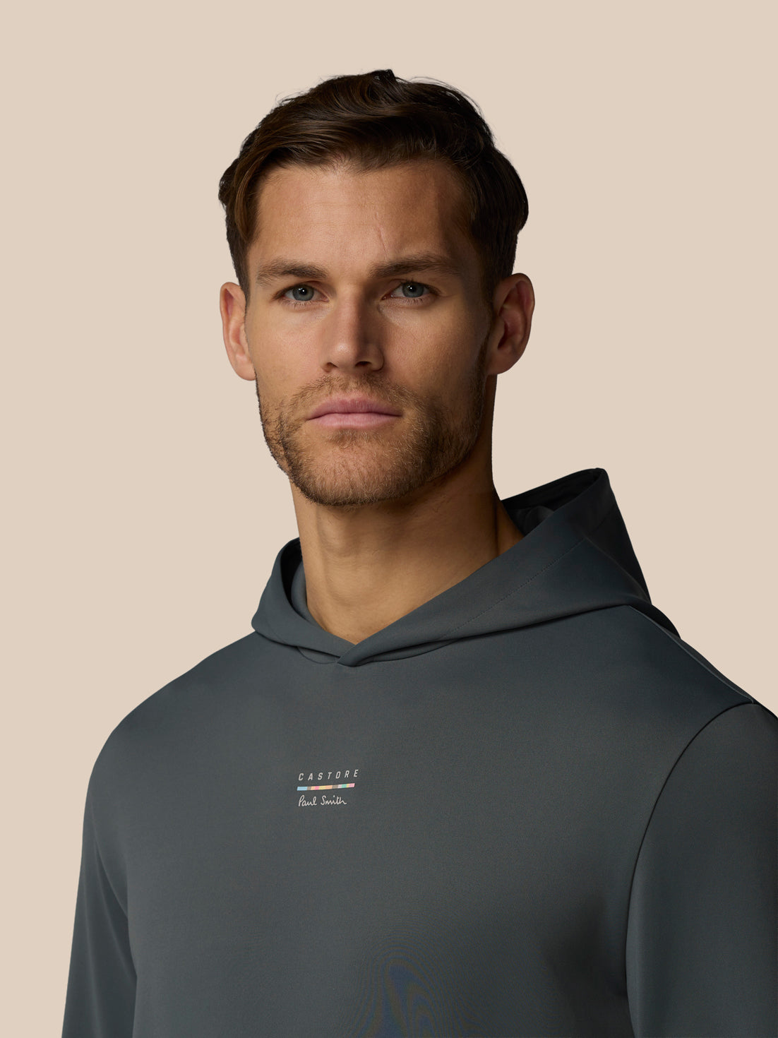 Man wearing a dark gray hoodie with a brand logo on a beige background