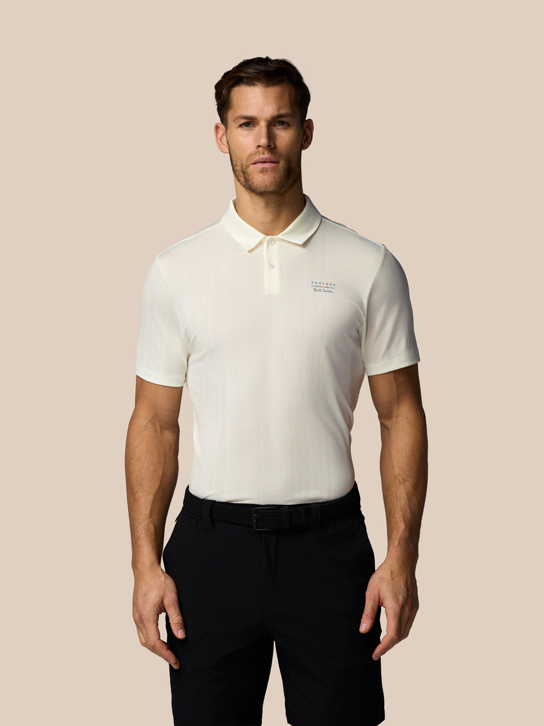 Man wearing a white polo shirt and black pants against a beige background