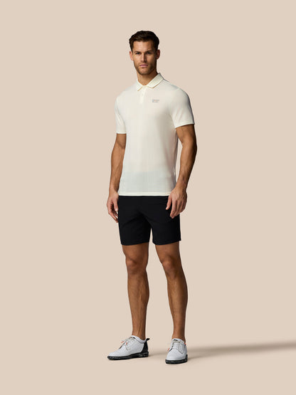 Man wearing a white polo shirt and black shorts on a beige background