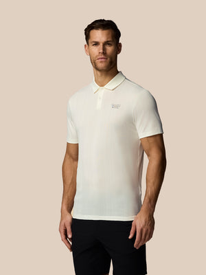 Man wearing a white polo shirt with a logo on a beige background