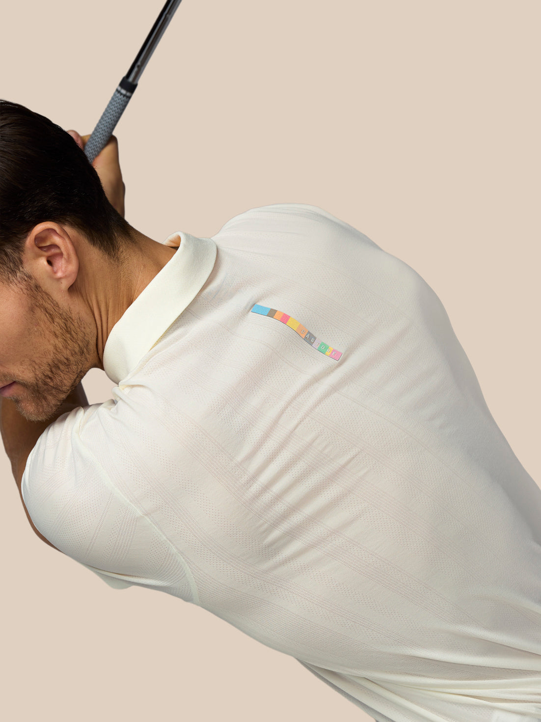 Man in a white polo shirt with a colorful logo on the chest, holding a golf club.