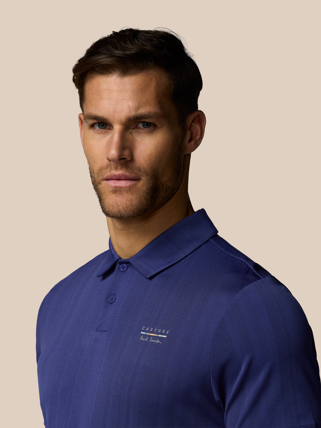 Man wearing a blue polo shirt with a brand logo on a beige background
