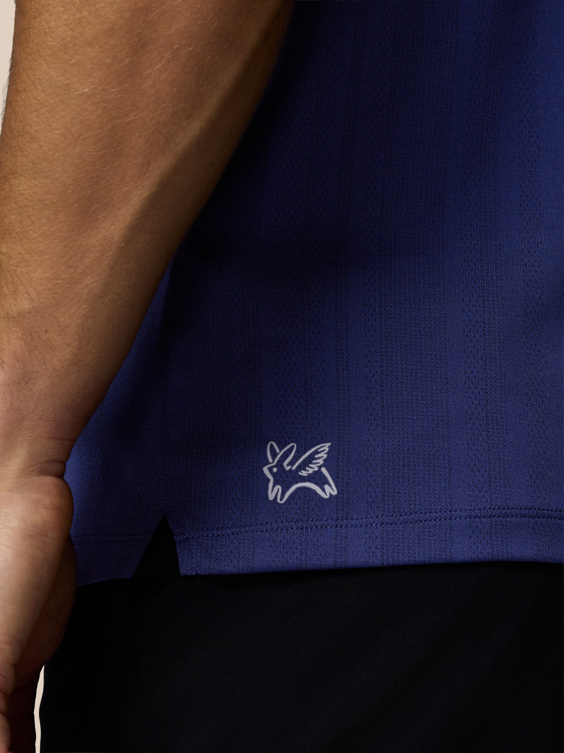 Close-up of a blue polo shirt with a white logo on a beige background