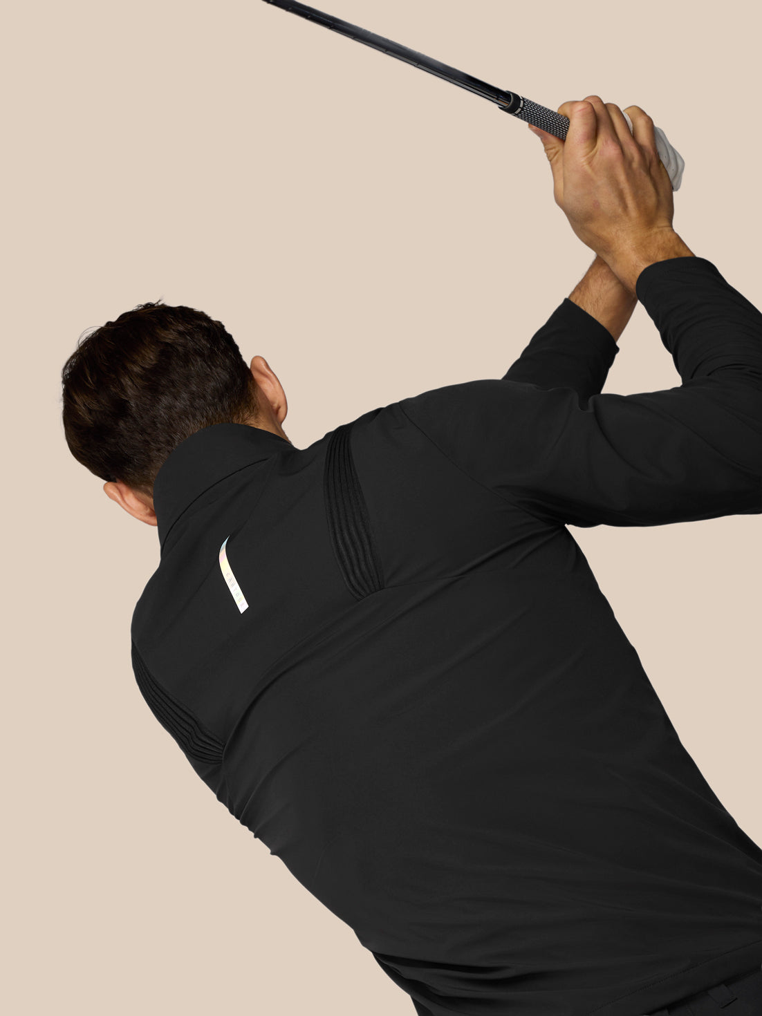 Man in black outfit swinging a golf club against a beige background