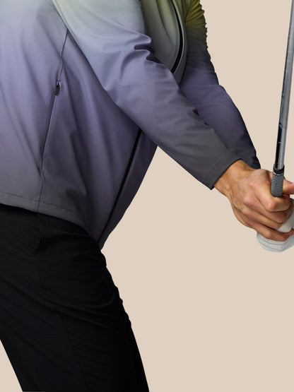 Person wearing a gray jacket holding a golf club on a beige background