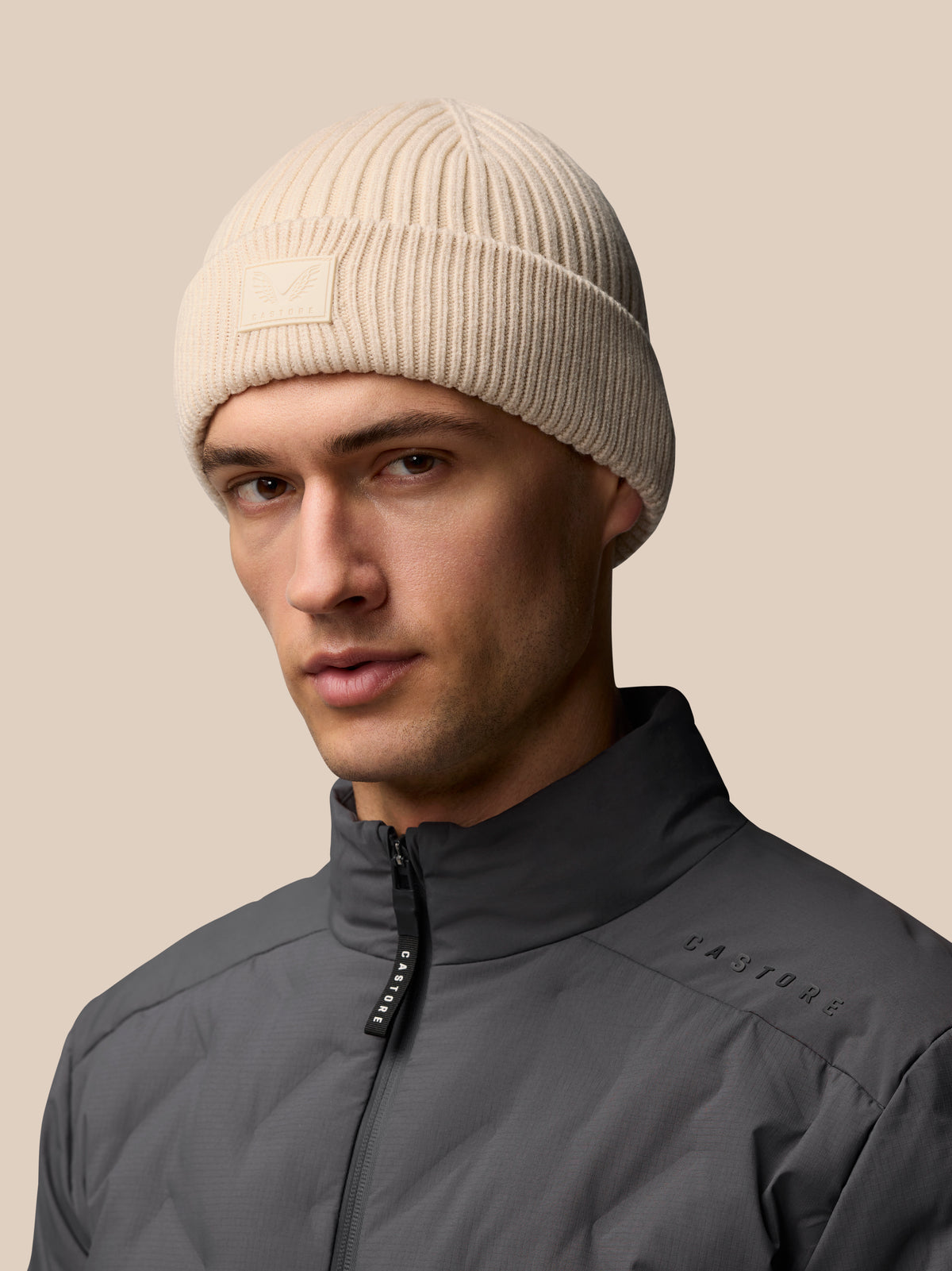 Stone colored ribbed knit Active Beanie with foldover Castore logo patch worn by a model.