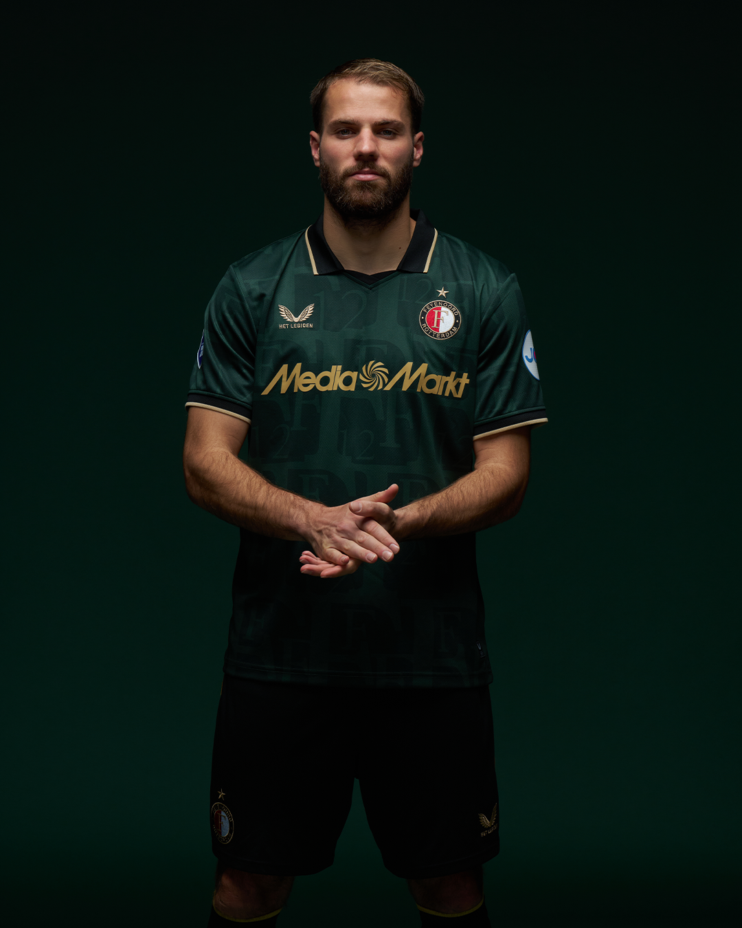 Male model wearing dark green Feyenoord football shirt with gold trim and crest, front view.