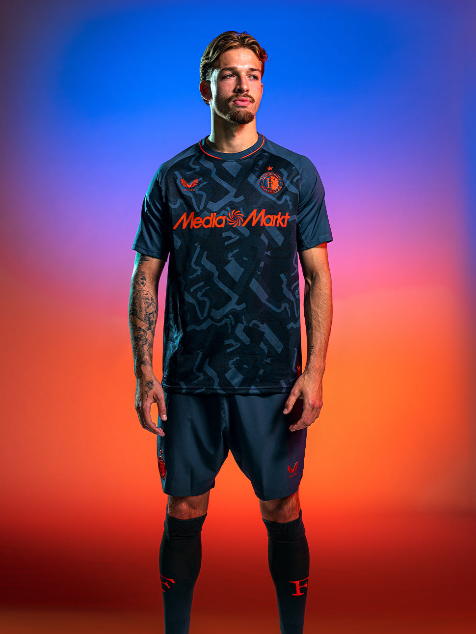 Male model wearing Feyenoord 2026-2027 third shirt in dark blue with orange detailing, Castore logo on right chest and Feyenoord crest on left chest.