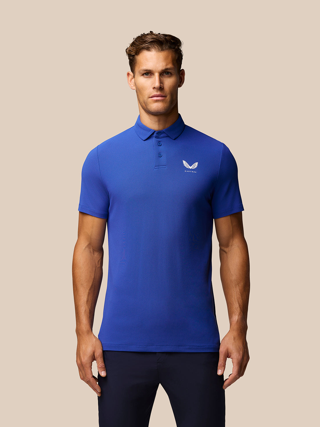 Male model wearing royal blue golf polo with three-button placket and Castore logo on the chest