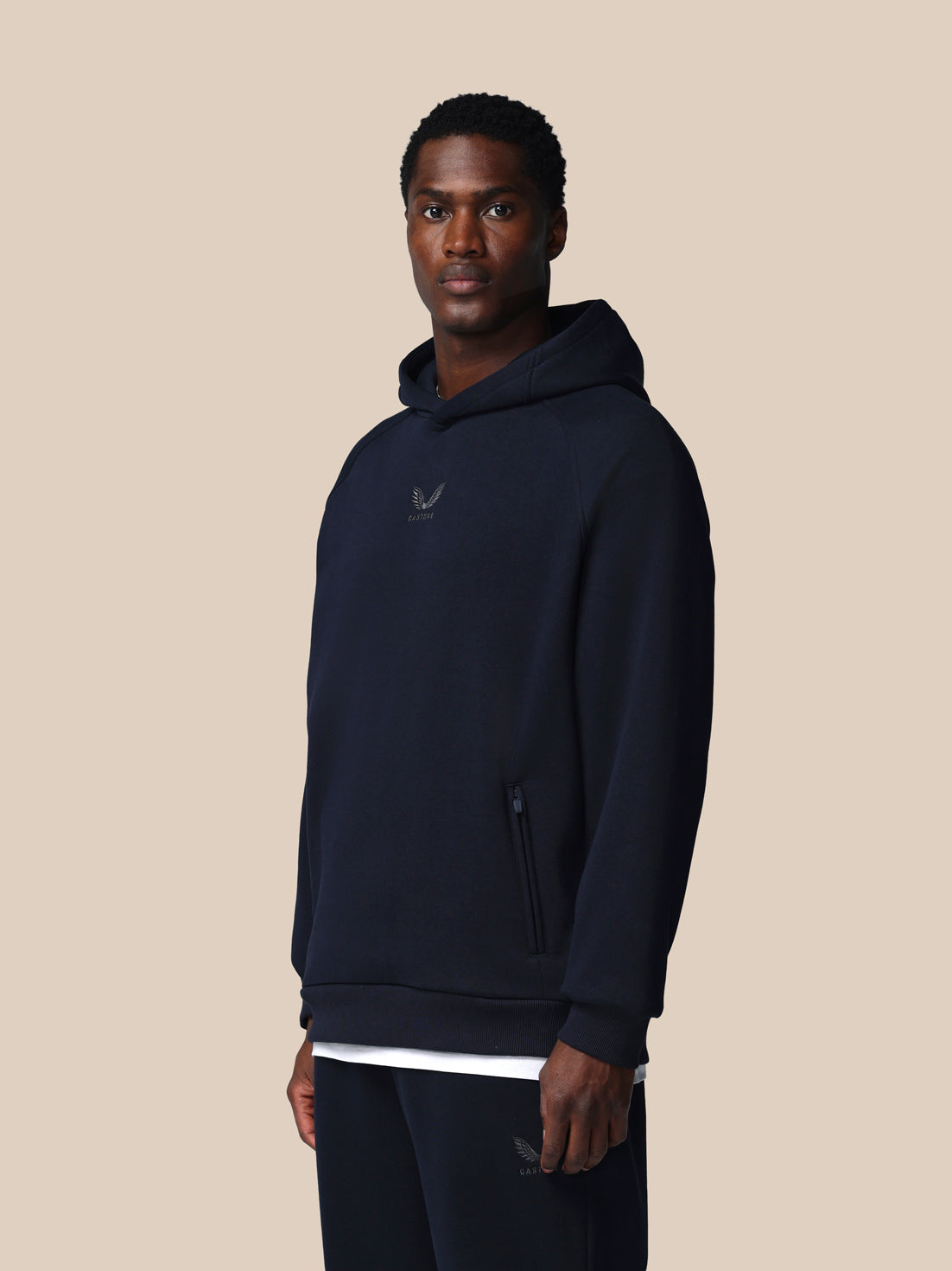 Man wearing a navy blue hoodie with a logo on a beige background